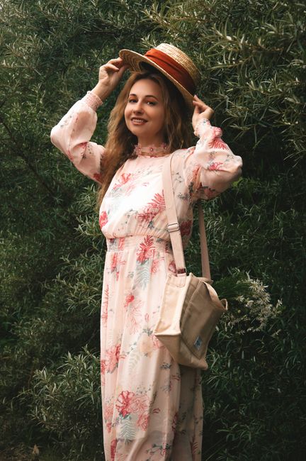 Smiling woman in floral dress and straw hat posing outdoors amid greenery. - handbag selection for seasons in Pakistan