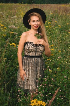 一位身穿蕾丝连衣裙、戴着帽子的妇女站在充满活力的田野里，手持鲜花