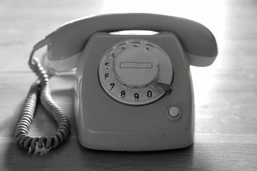 High contrast black and white image of a vintage rotary phone on a wooden surface emphasizing nostalgic communication.