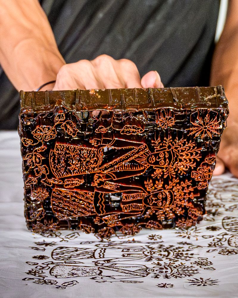 Hands pressing a carved wooden block onto fabric