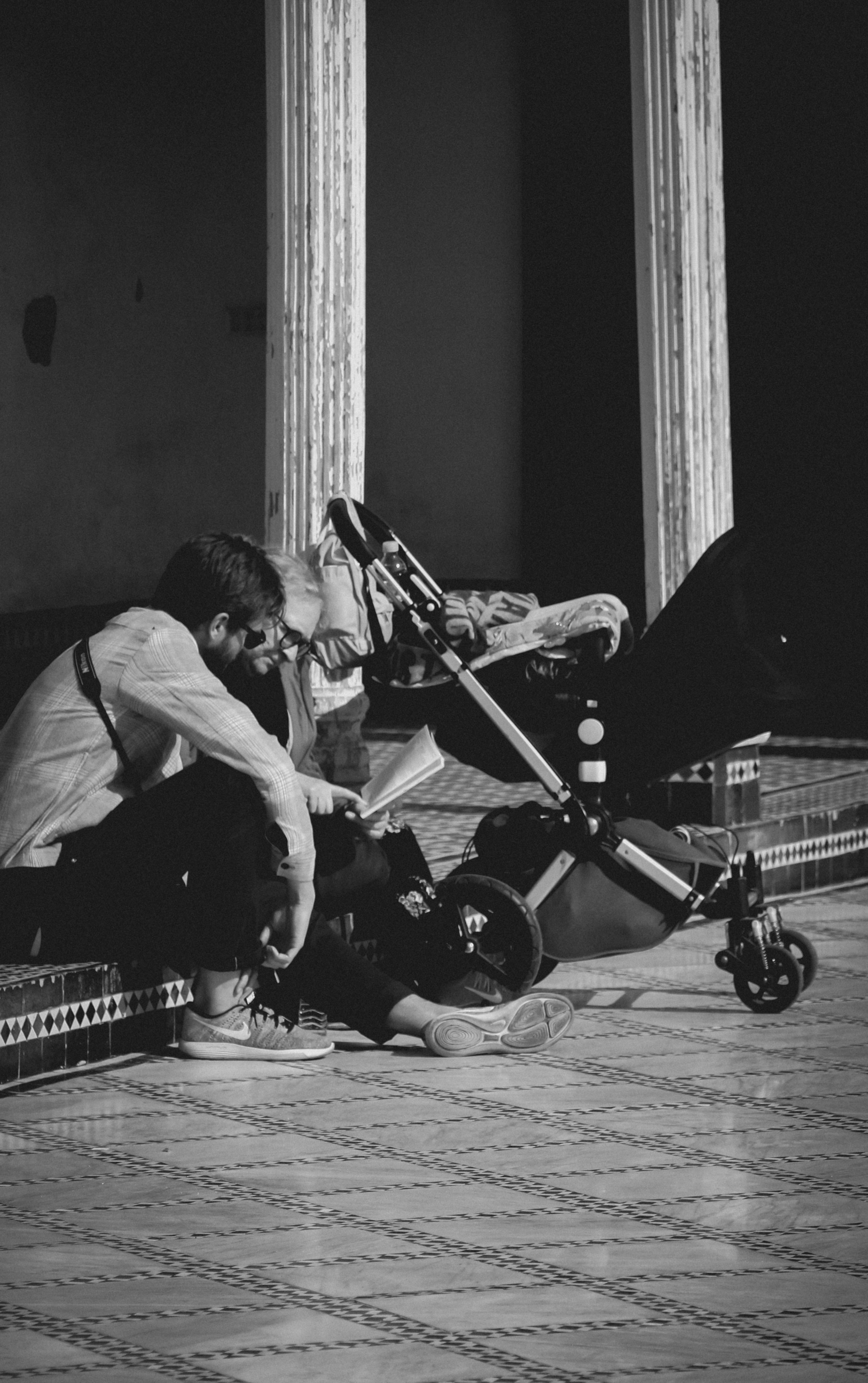 bezplatná Černobílá fotografie dospělého a dítěte sedících vedle kočárku, zachycující tichou, introspektivní scénu. Základová fotografie