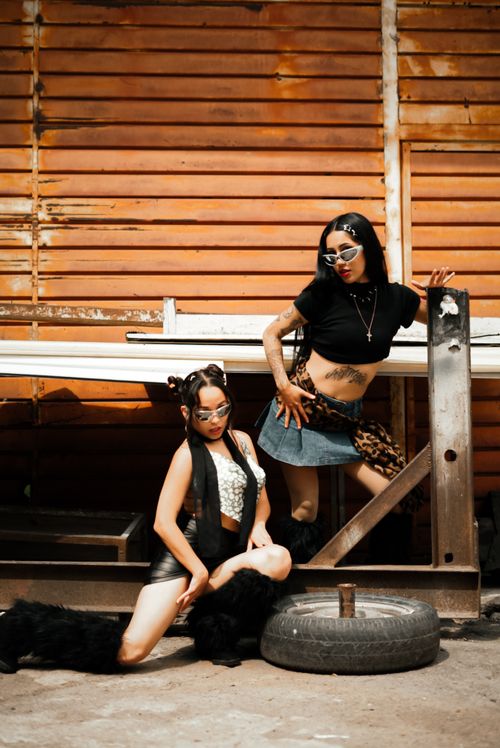 Free Stylish photoshoot featuring two women in modern urban outfits against a warehouse backdrop. Stock Photo