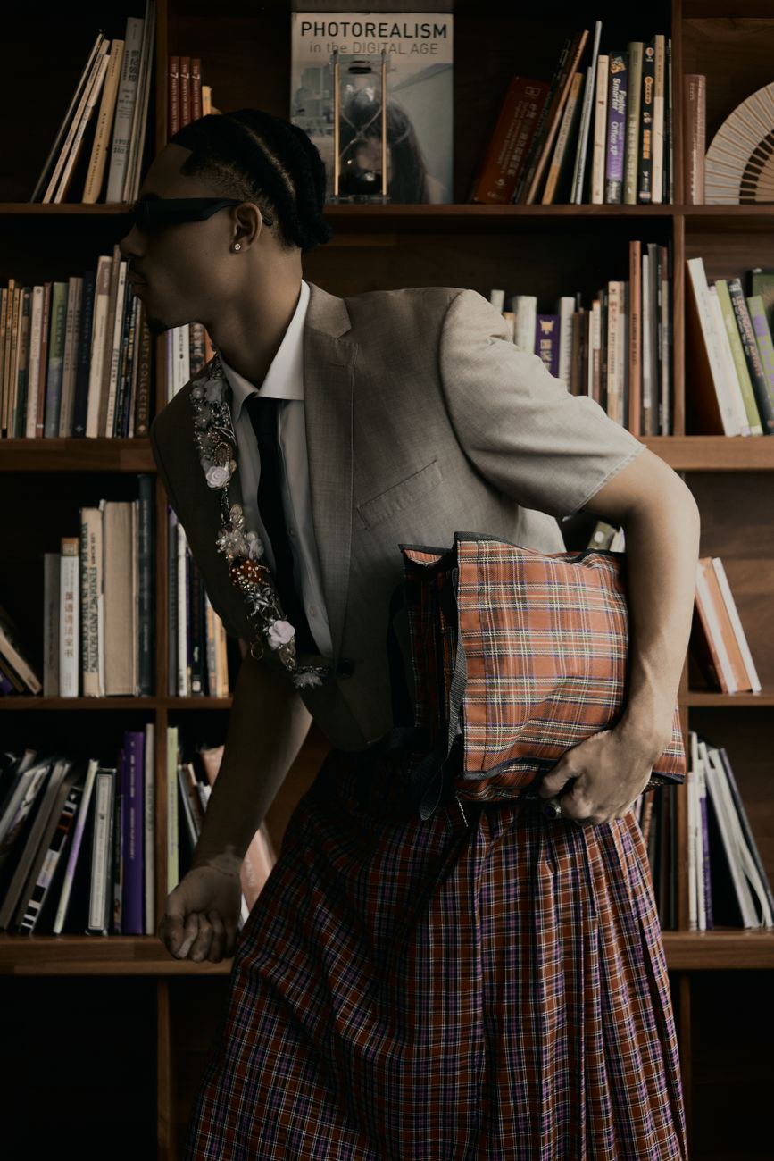 A stylishly dressed reader moving through a library with a plaid bag over one shoulder