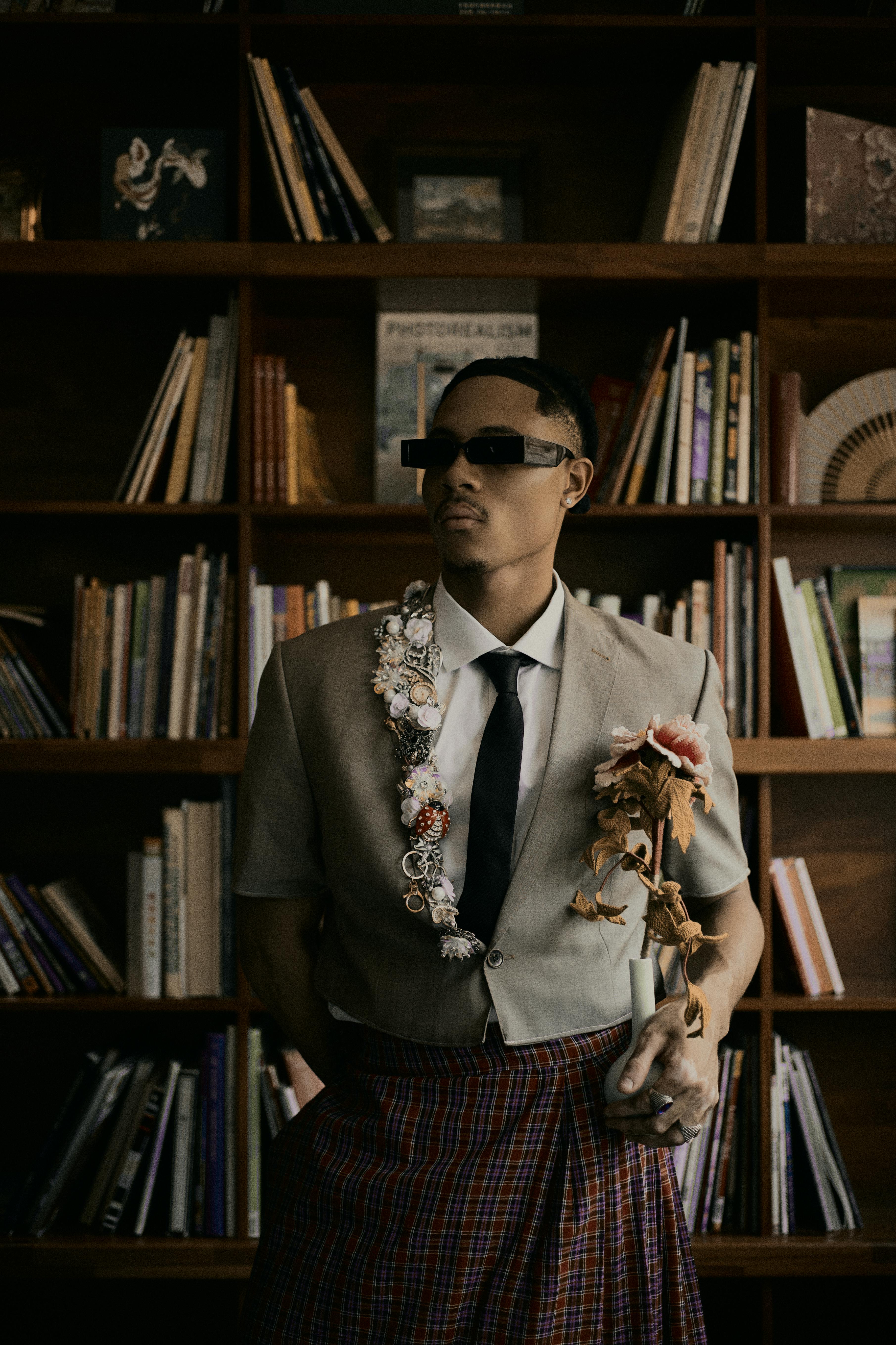 Gratis Un uomo elegante, con un abbigliamento unico, posa in una moderna biblioteca con scaffali. Foto a disposizione