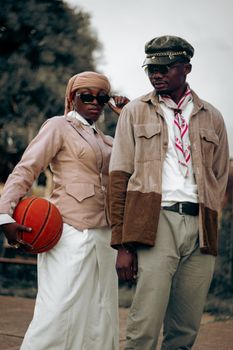 Elegant couple posing outdoors in chic vintage attire with a basketball.