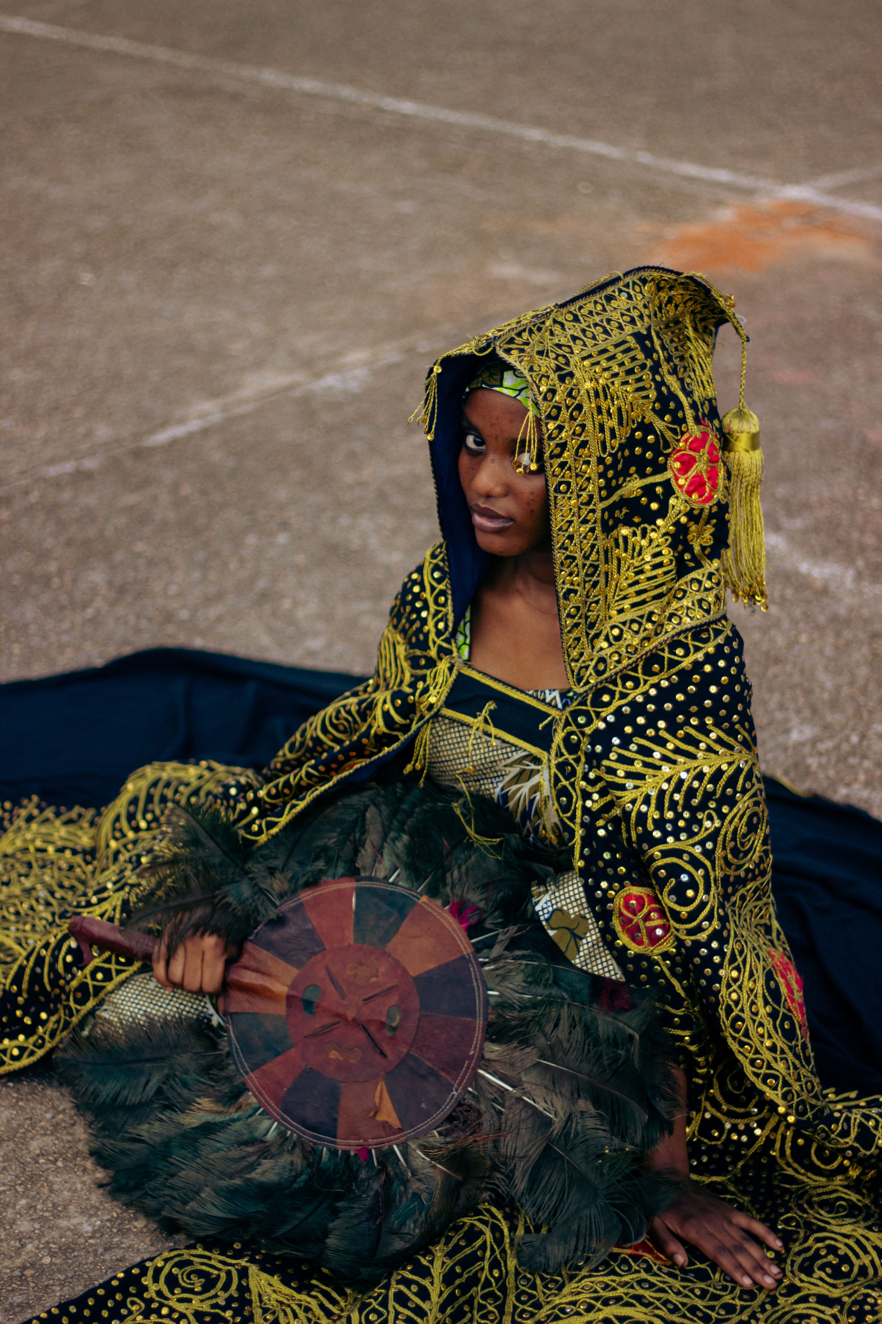 Portrait of an African woman in intricate traditional clothing holding a drum, set outdoors.