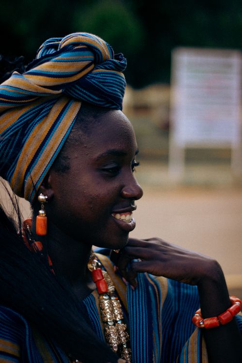 Free Woman in vibrant traditional African attire with jewelry, smiling outdoors. Stock Photo
