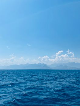 Calm ocean waves under a clear blue sky with distant mountain vistas.