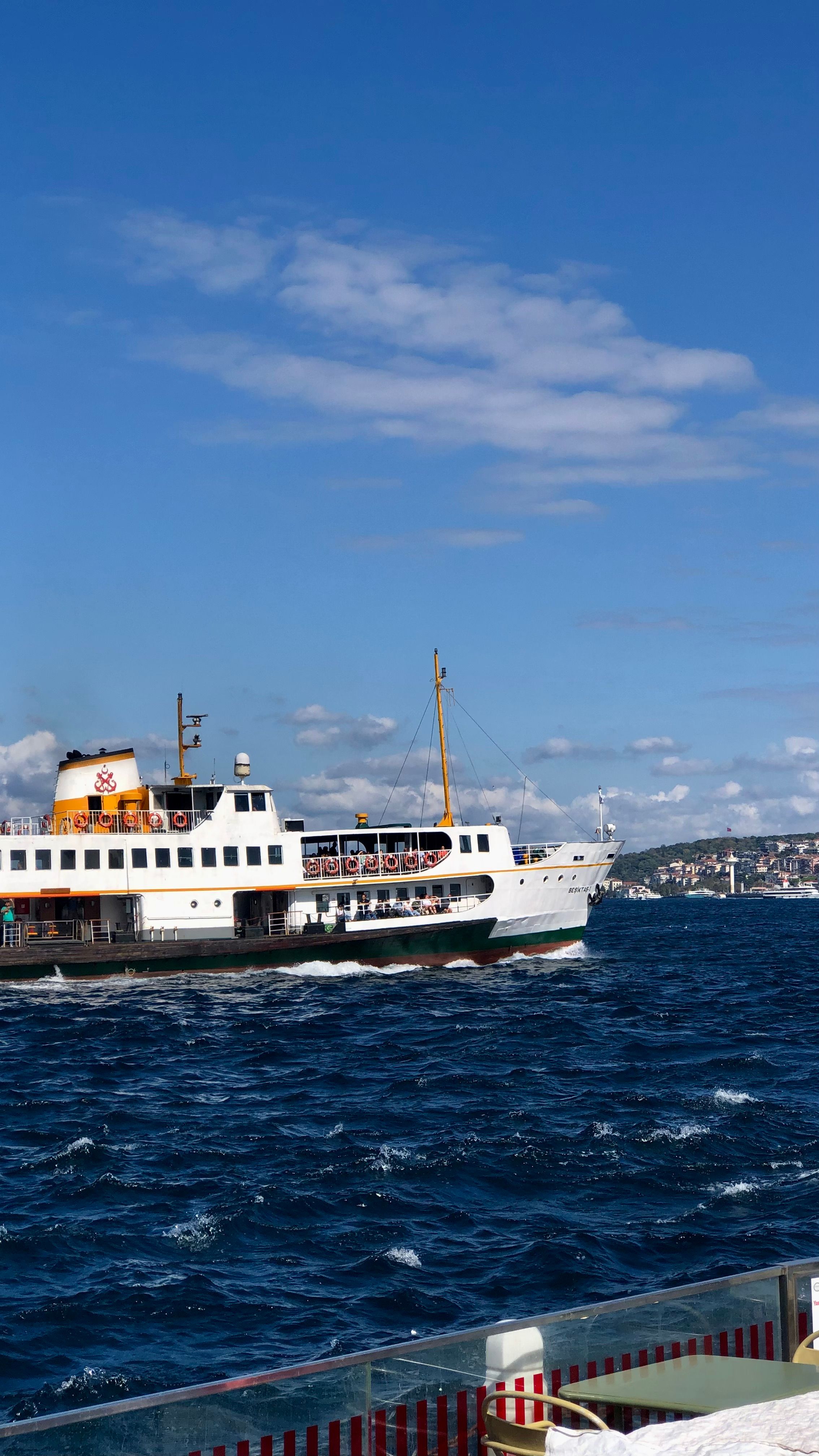 Ferry cruising on the sea under a clear blue sky with city skyline in the background.