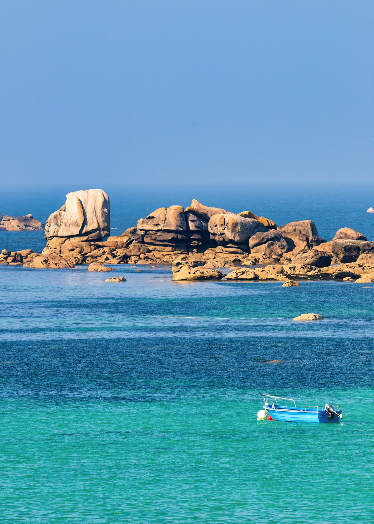 Rose granite boulders and turquoise water with a lone blue boat
