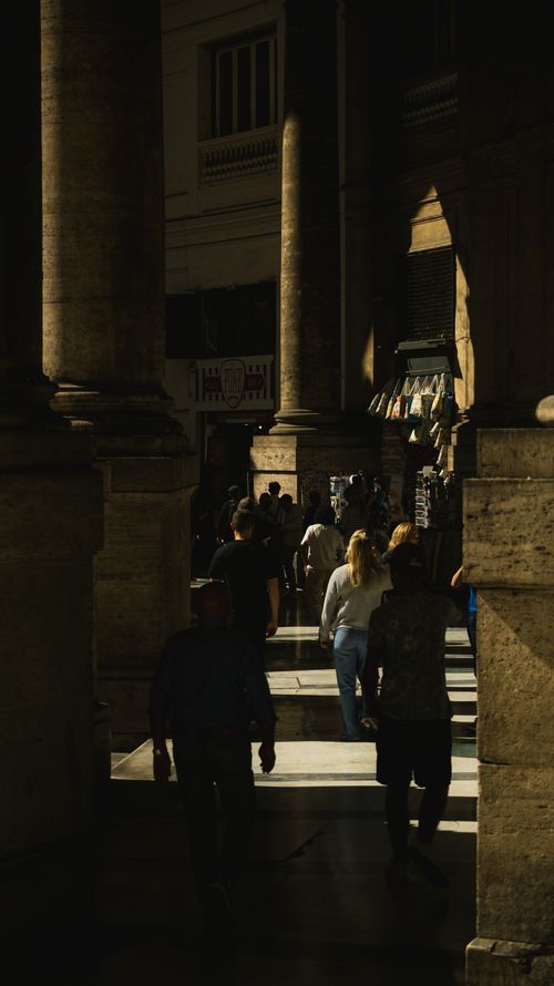 Free A bustling Italian arcade with people walking under ancient arches on a sunny day. Stock Photo