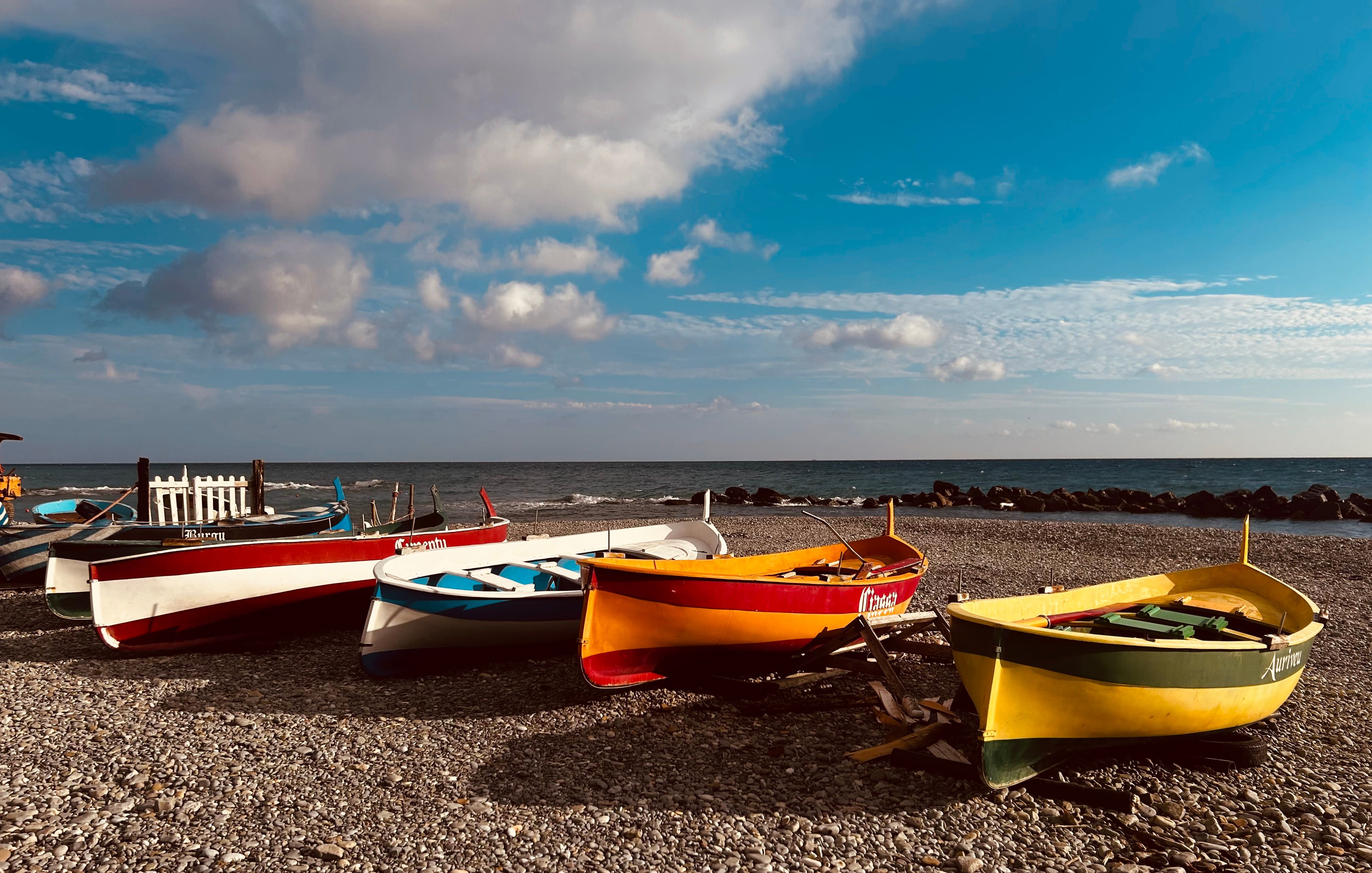 Colorful Boats on a Pebble Beach Under Blue Skies · Free Stock Photo