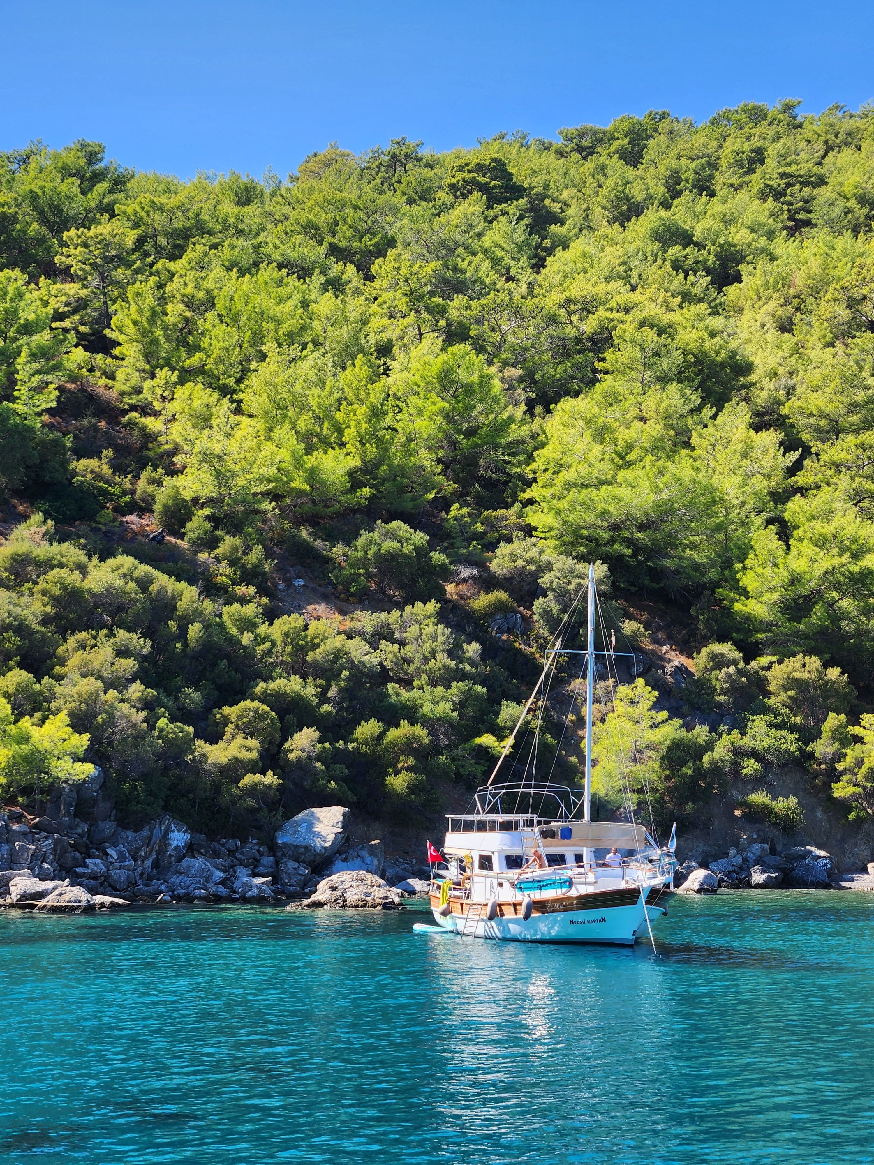 A sailing yacht at anchor in a clear turquoise cove