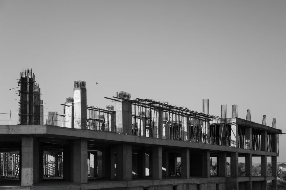 Exposed rebar rising from unfinished concrete columns and slabs of a Mediterranean building at dusk