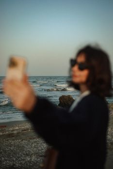 A fashionable young woman takes a selfie by the sea at sunset in Baku, capturing the vibrant and relaxed atmosphere.