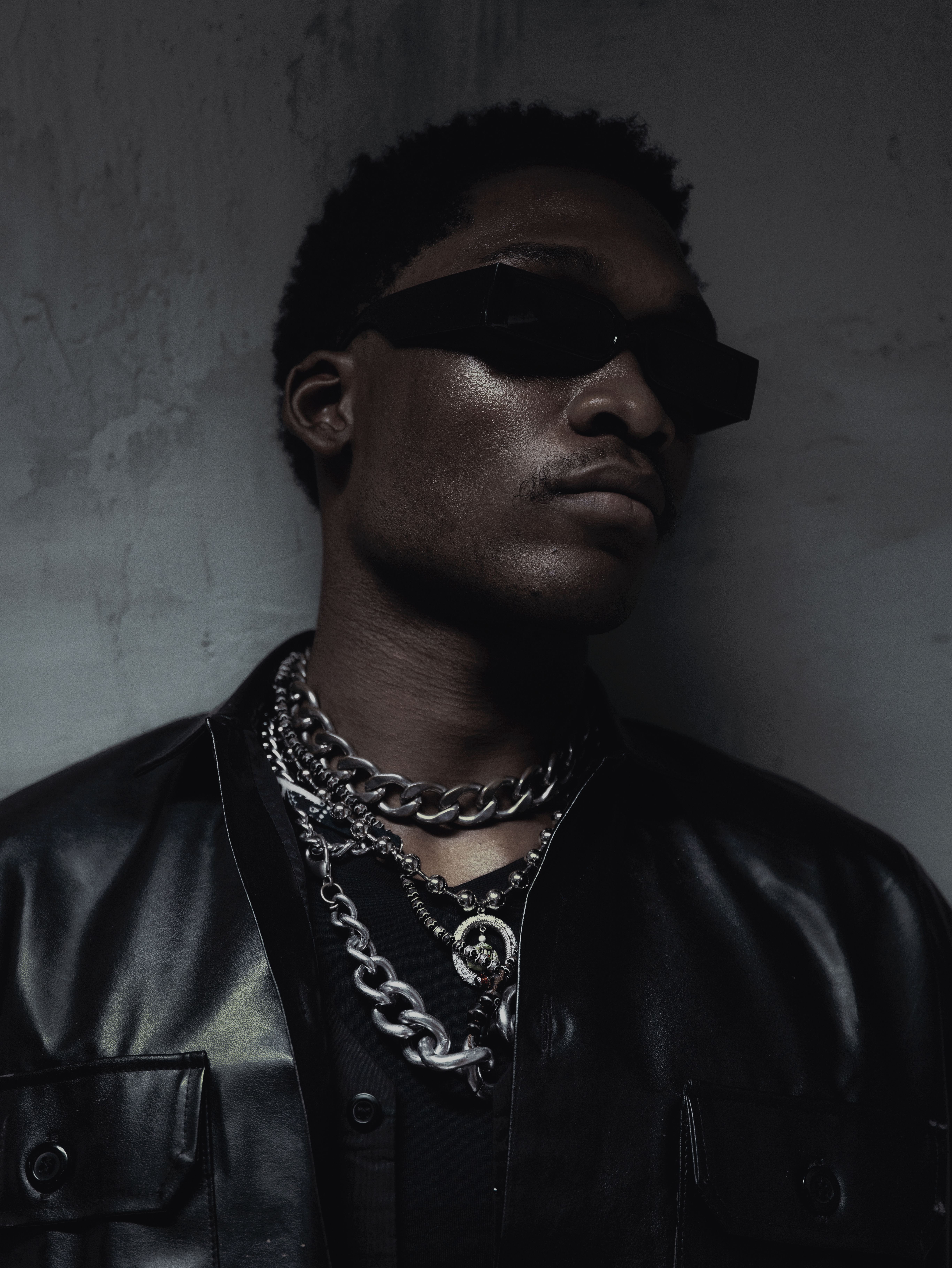 Edgy fashion portrait of a man wearing sunglasses and chains, exuding confidence.