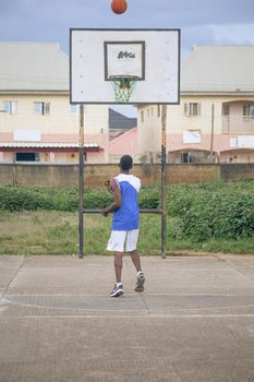 A young black male playing basketball on an outdoor court, captured mid-shot.