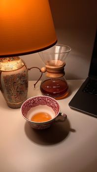 Warm desk scene with a cup of coffee, lamp, and laptop, creating a cozy atmosphere.