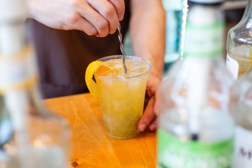 Free Close-up of a barista stirring a refreshing citrus drink with ice and orange garnish. Stock Photo