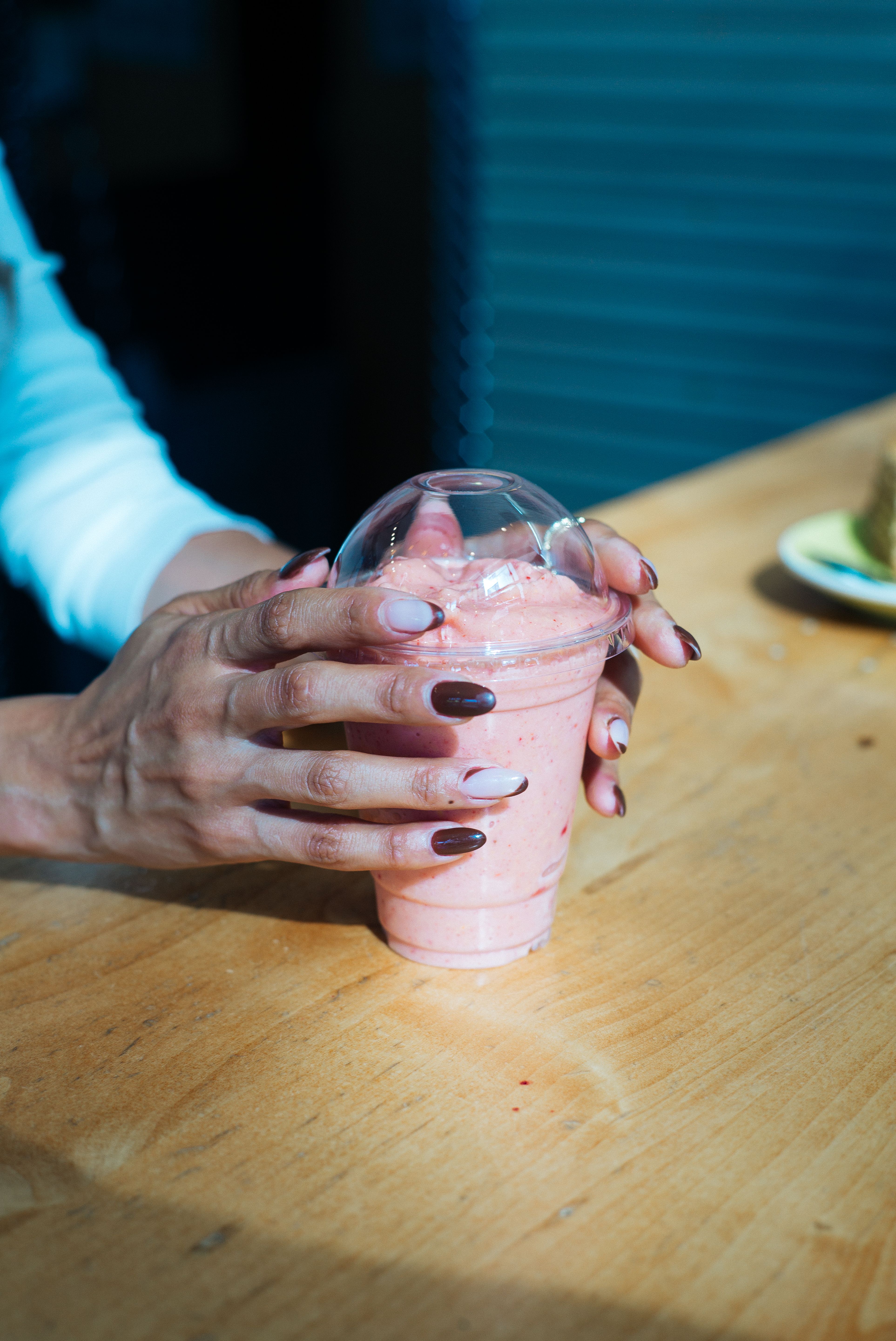 Close-up of hands holding a strawberry smoothie in a clear cup indoors.
