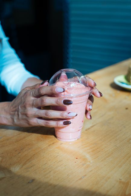 Close-up of hands holding a strawberry smoothie in a clear cup indoors.