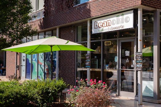 Cozy coffee shop with green outdoor umbrella and vibrant garden in a sunny setting.