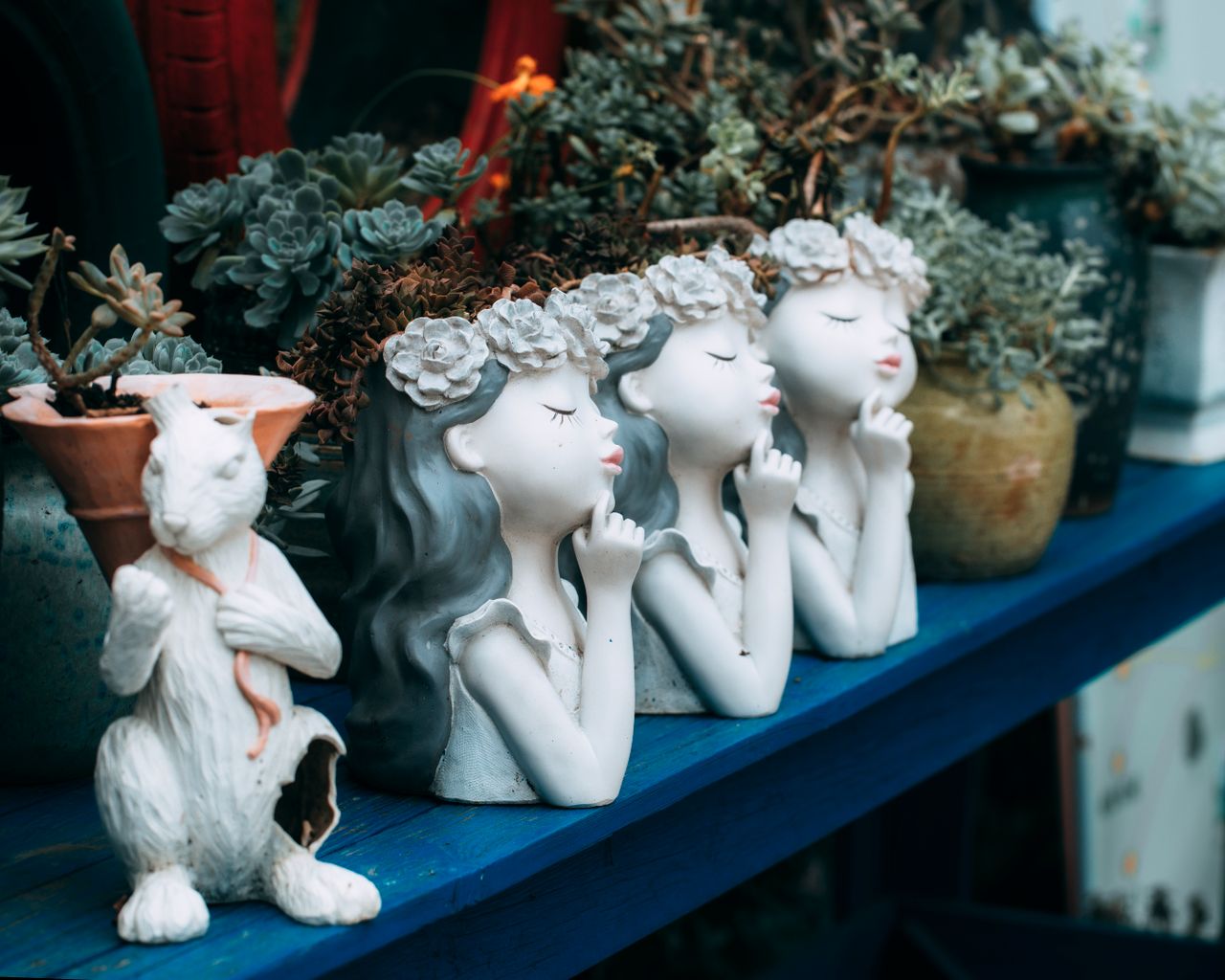 whimsical garden statues with floral crowns among succulents create an