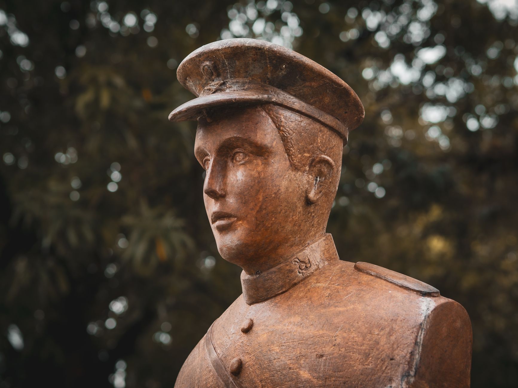 Close-up of a bronze soldier statue with a detailed uniform and cap, set against a leafy background.