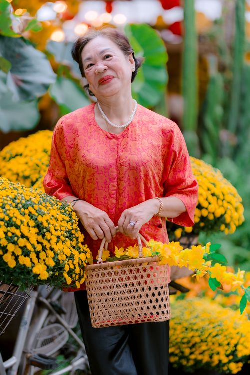 Free Smiling elderly woman holding a basket among vibrant yellow flowers in a garden setting. Stock Photo