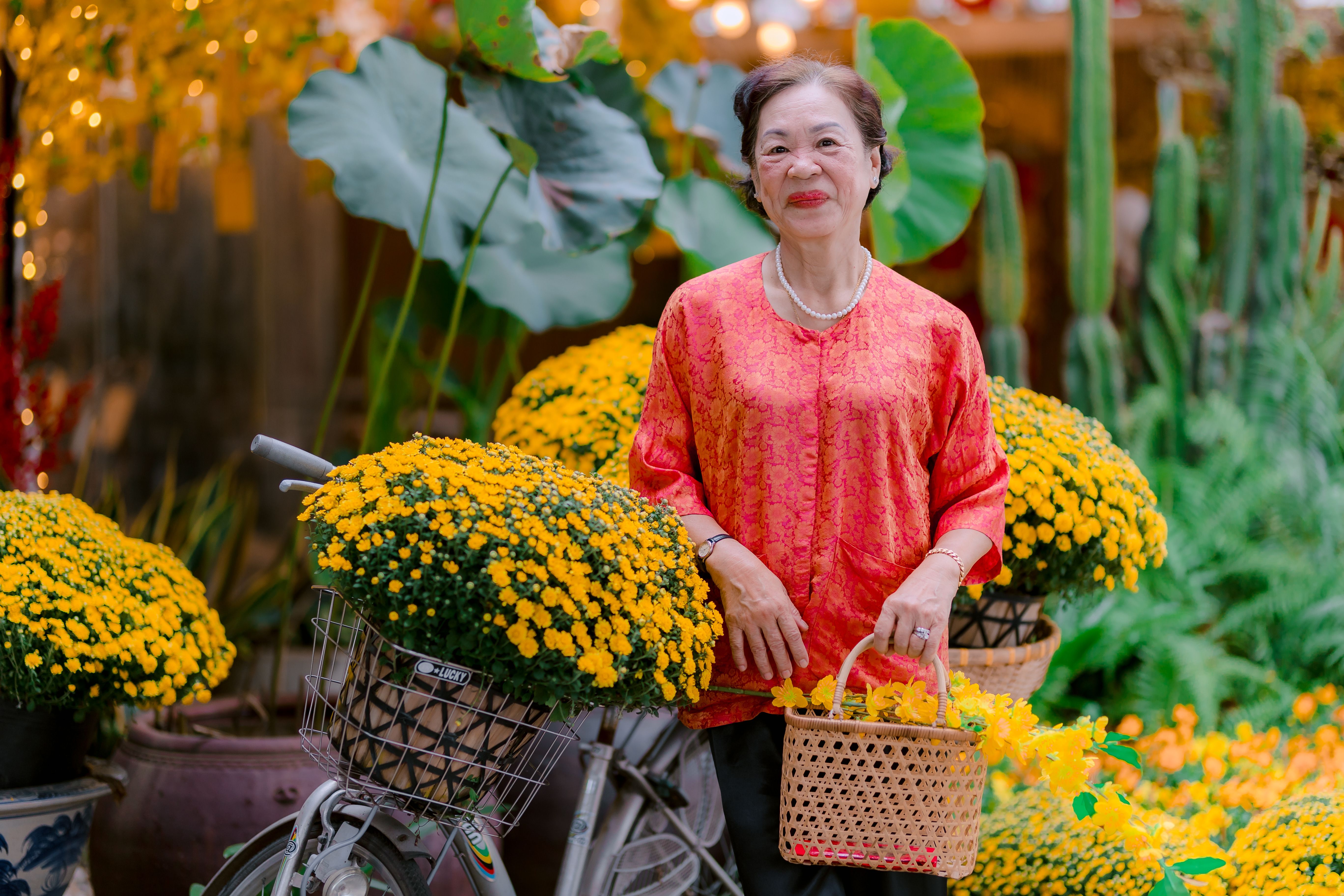 Elderly woman standing with a bicycle adorned with yellow chrysanthemums, smiling warmly.