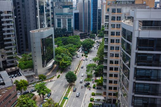 Aerial view of a bustling city street lined with modern skyscrapers and green trees.
