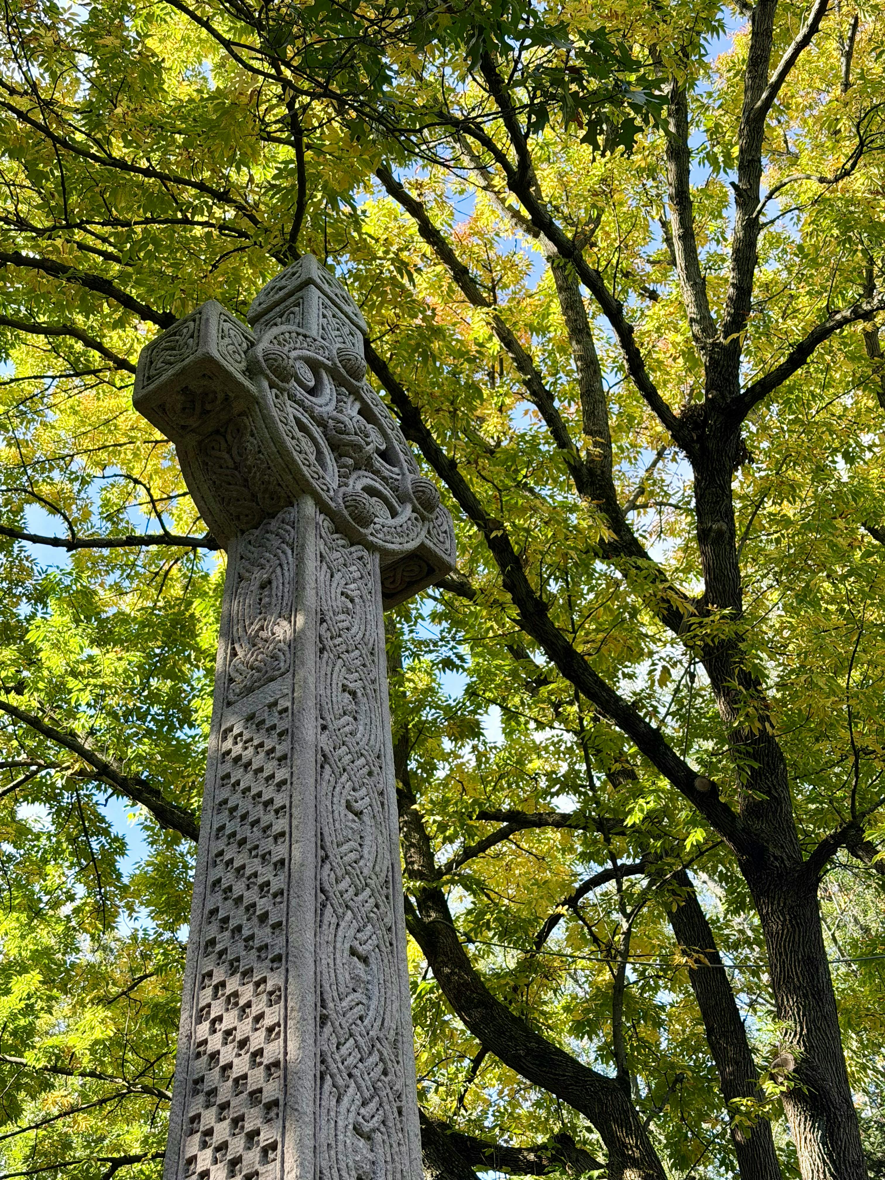 Detailed Celtic cross with intricate knotwork carvings standing outdoors against a grey sky