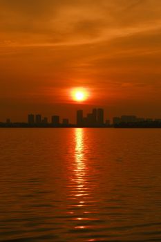 Orange sunset reflecting on water with an urban skyline silhouette in Japan.