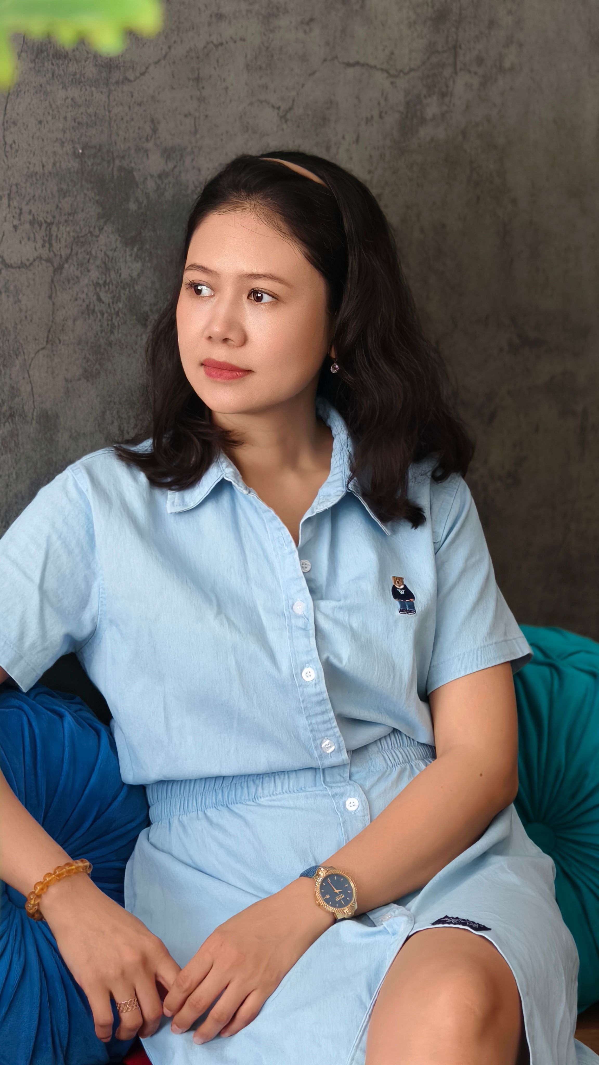 A serene portrait of a woman in a light blue dress sitting indoors, offering a calm and relaxed vibe.