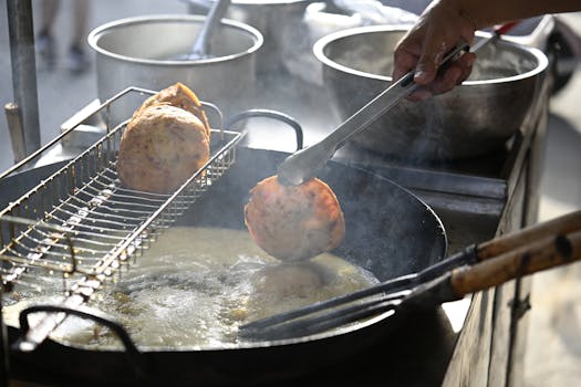 Street vendor frying food balls in hot oil, using tongs at an outdoor market.