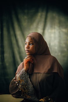 Portrait of a woman wearing a brown hijab and traditional henna, looking contemplatively to the side.