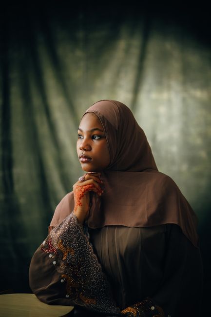 Portrait of a woman wearing a brown hijab and traditional henna, looking contemplatively to the side.
