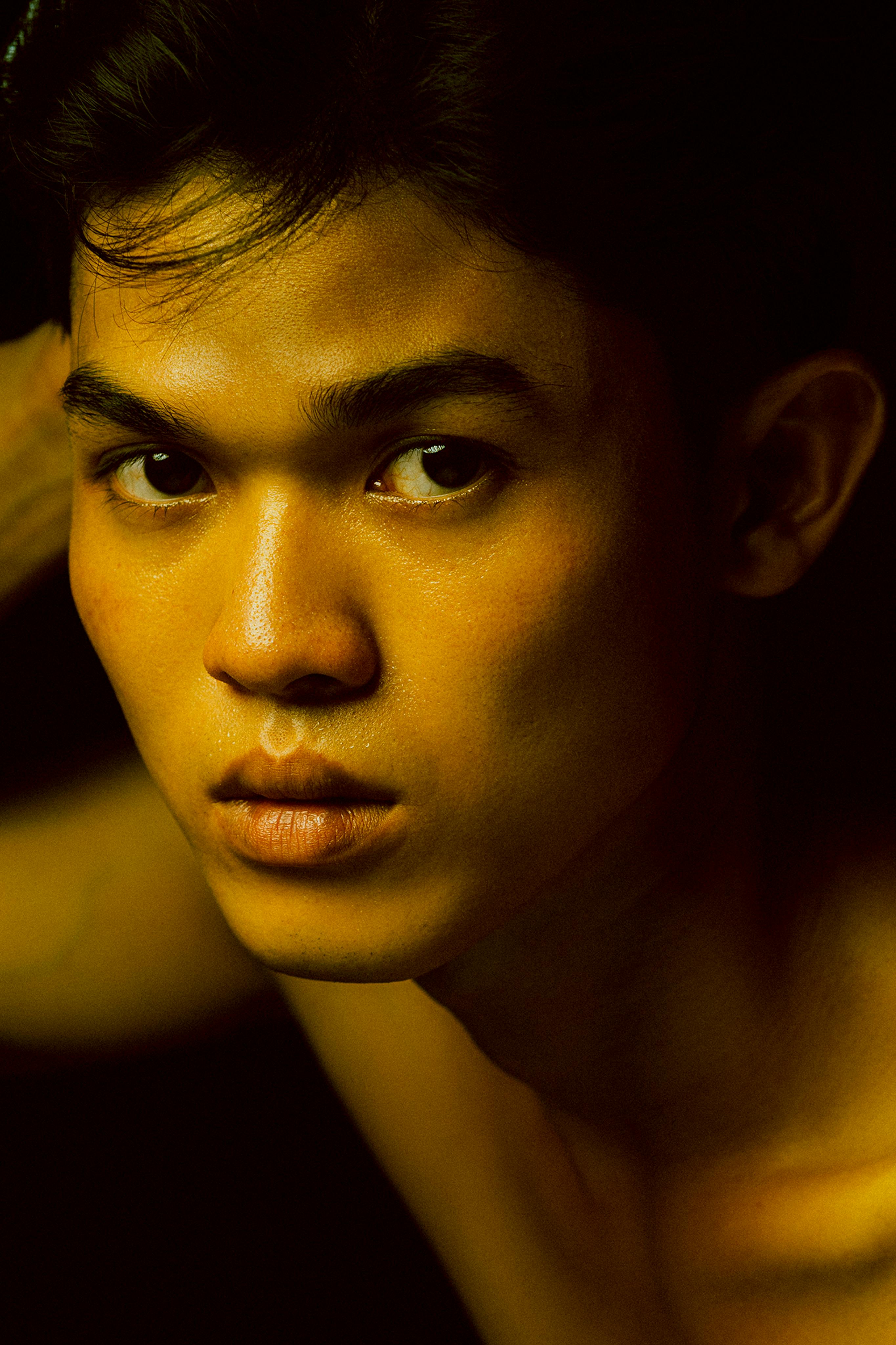 Close-up portrait of a young man in low light with dramatic shadows.