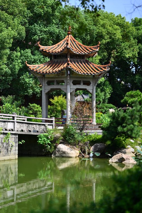 Free Serene image of a traditional Chinese pavilion reflected in a pond, surrounded by lush greenery. Stock Photo
