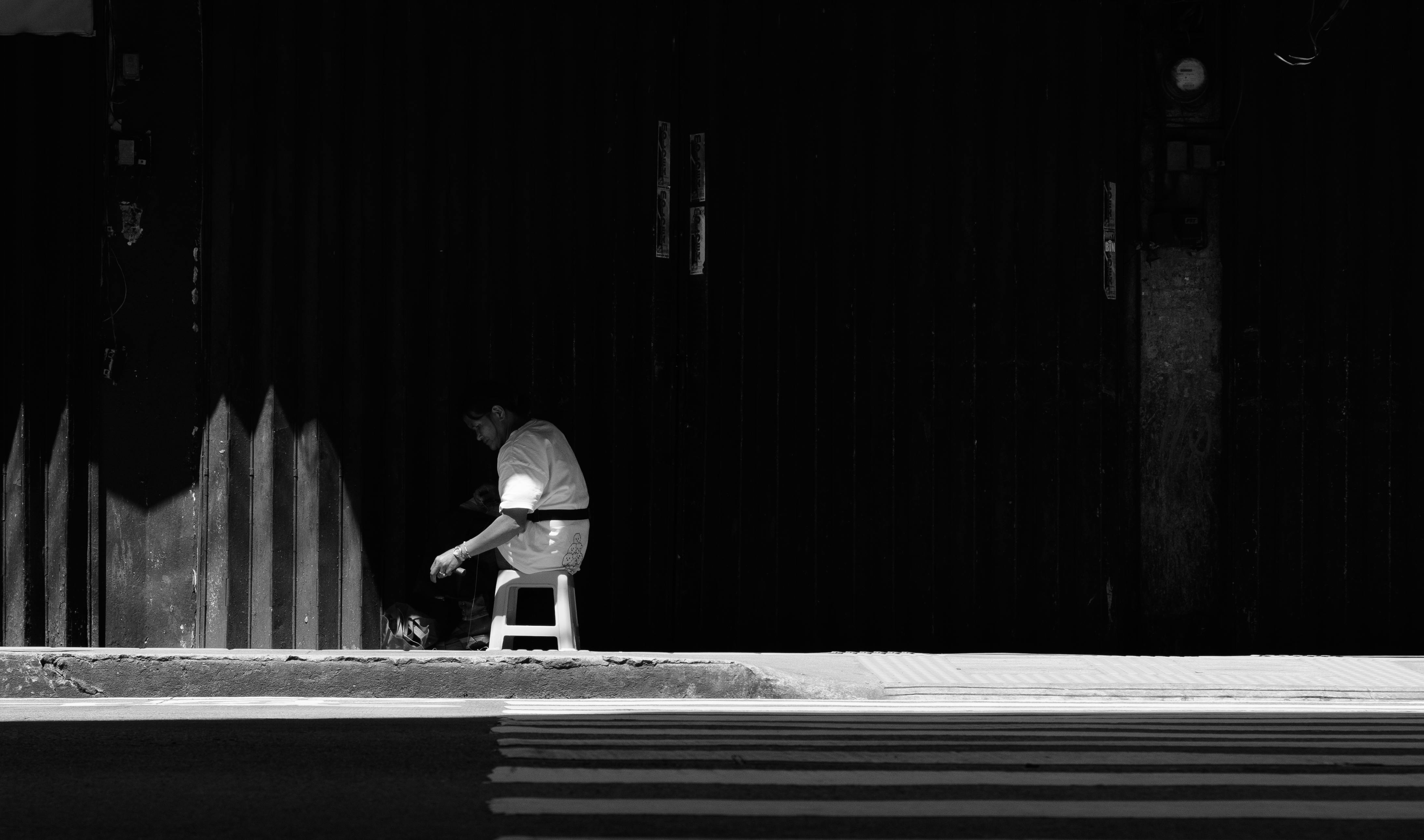 De franc Una persona solitària seu a l'ombra en una dramàtica escena de carrer en blanc i negre. Foto d'estoc