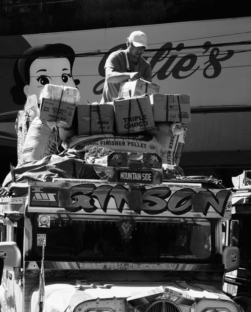 Free Man loading packages onto a jeepney in Baguio, Philippines, showcasing urban street life in black and white. Stock Photo
