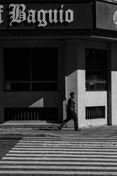High-contrast black and white photo capturing a lone man walking past a building in Baguio City.. pexels, high, contrast