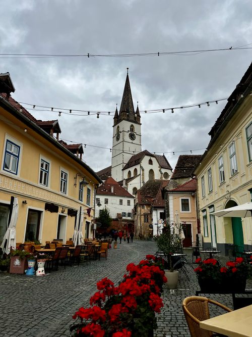 Free Picturesque European street with a historic church tower under a cloudy sky. Stock Photo