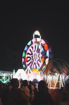 Vibrant Ferris wheel with colorful lights spinning at a night carnival, creating a lively atmosphere.