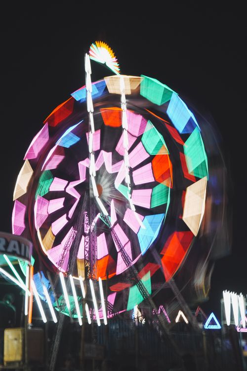 Free Colorful Ferris wheel spinning under bright lights at a night carnival, creating a festive atmosphere. Stock Photo
