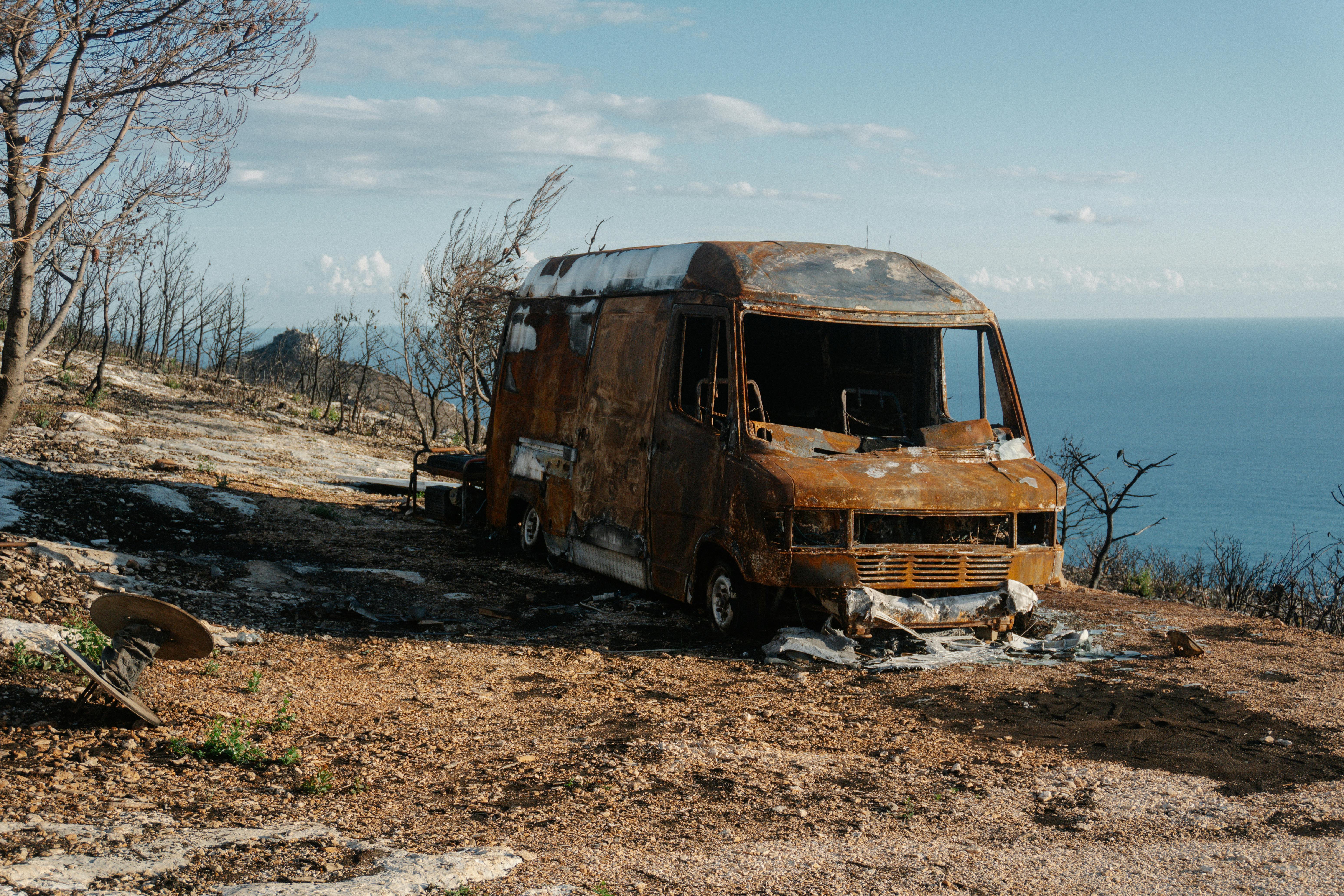 一辆烧毁的面包车停在崎岖的山上，可以看到美丽的海景