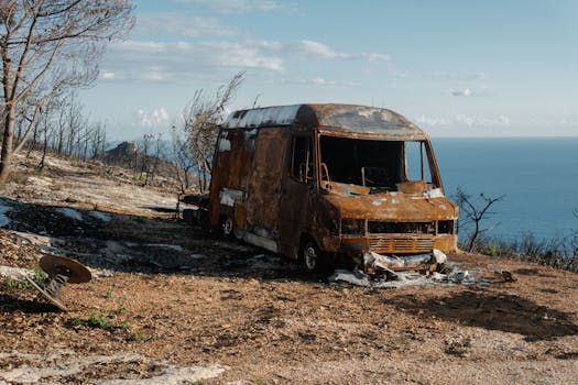 一辆烧毁的面包车停在崎岖的山上，可以看到美丽的海景