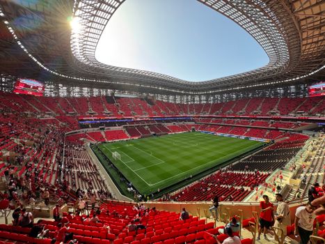A modern football stadium with red seats, filled with fans during a daylight match, showcasing architectural design.
