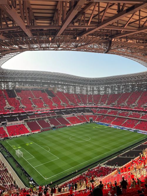 Free Aerial view of a modern football stadium, showcasing vibrant red seating and a lush green field. Stock Photo