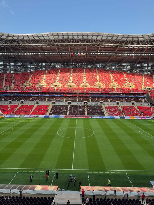 Free A lively football stadium under clear skies with red and black seating filled with spectators. Stock Photo